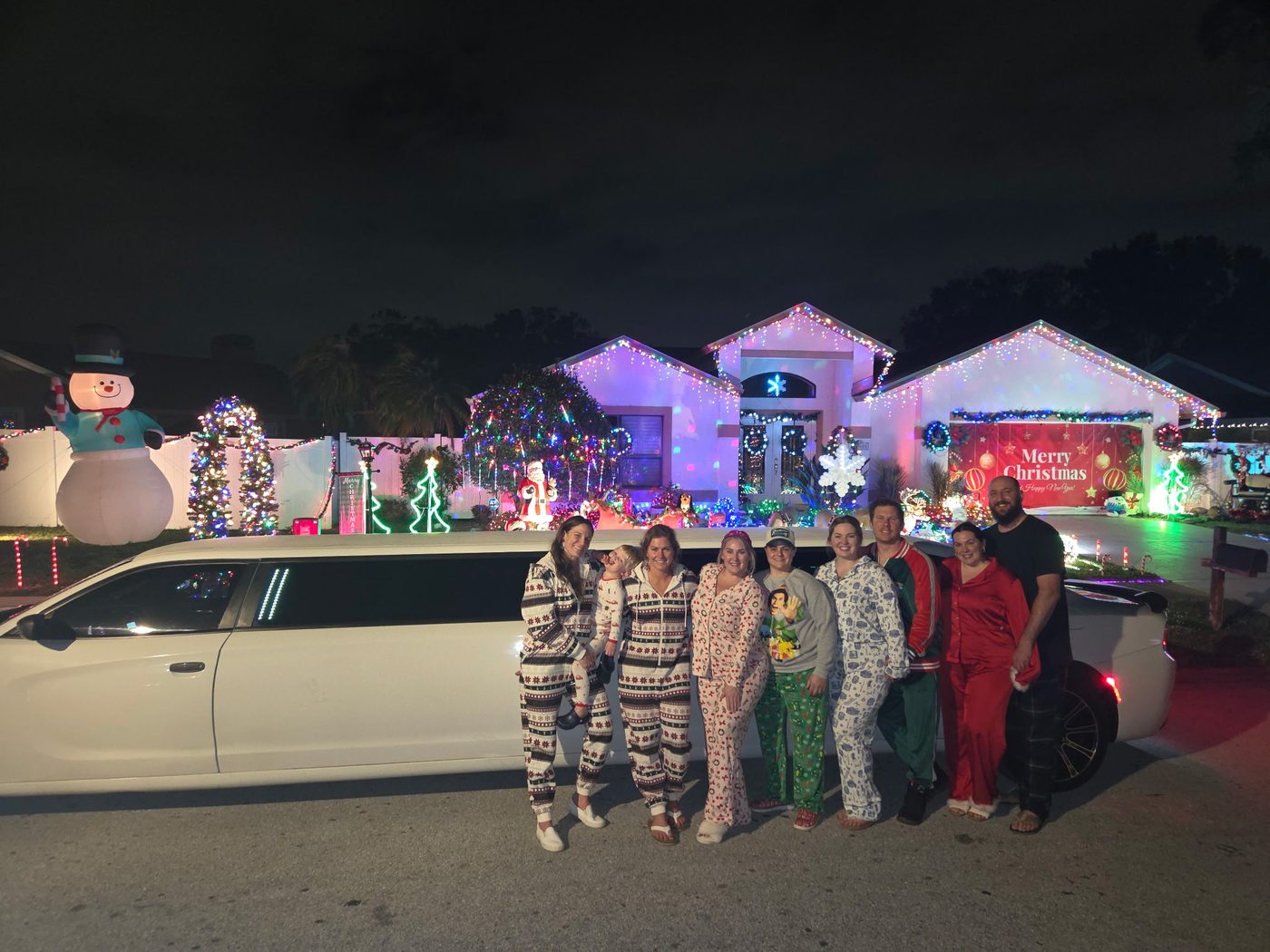 Family in holiday pajamas by the Big Time Limo at a Christmas-lights house